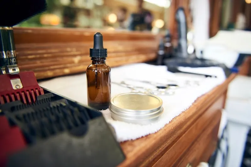 A barber's station: beard oil, clippers and a folded towel on the counter
