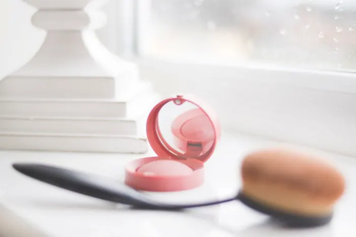 A blush compact and brush on a white shelf